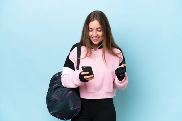 Young sport woman with sport bag isolated on blue background surprised and sending a message - Foto, Bild