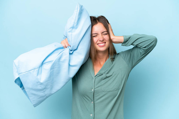 Young beautiful woman isolated on blue background in pajamas and holding a pillow stressed overwhelmed - Photo, Image