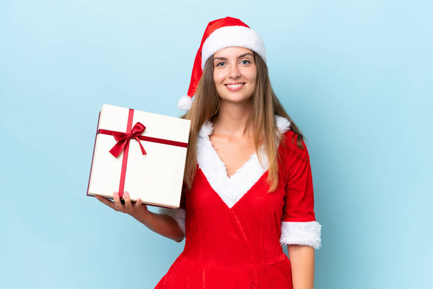 Anne Noel gibi giyinmiş, mavi arka planda izole edilmiş bir hediye taşıyan beyaz bir kadın. - Fotoğraf, Görsel