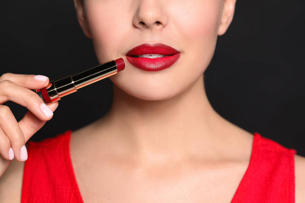 Young woman with beautiful makeup holding red lipstick on black background, closeup - Φωτογραφία, εικόνα