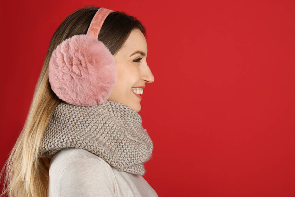 Happy woman wearing warm earmuffs on red background, space for text - Foto, afbeelding