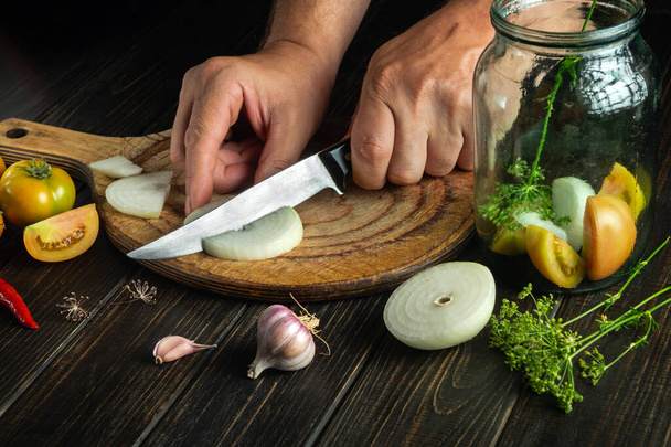 Кухар розрізає цибулю на обробній дошці ножем. Приготування смачних маринованих помідорів в домашніх умовах
 - Фото, зображення