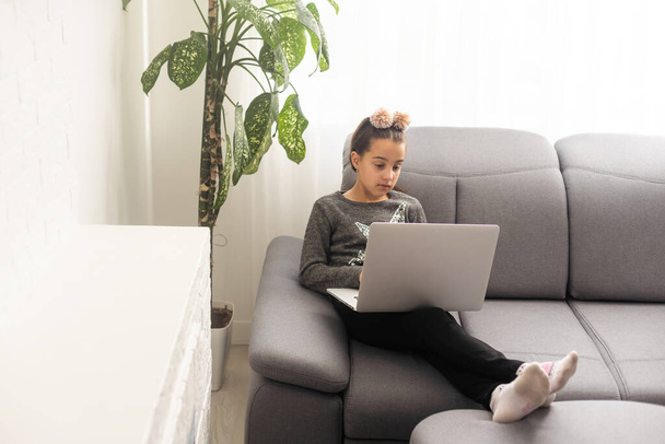家庭でノートを作るからオンラインで勉強10代の女の子の学校の生徒。10代の学生の距離は、ノートパソコンで宿題をしたり、ビデオレッスンを見たりします。遠隔教育の概念. - 写真・画像