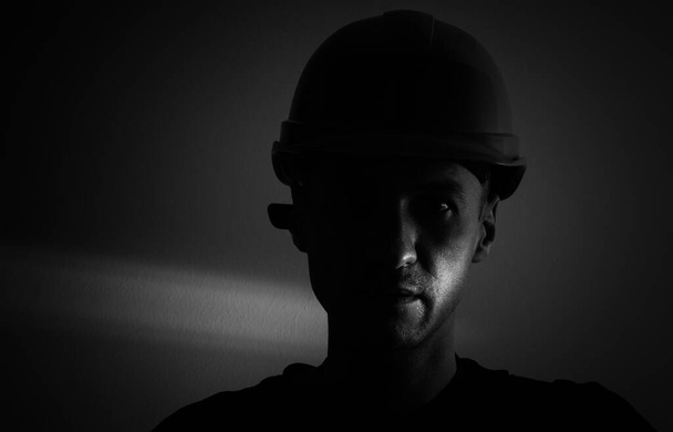 Cara sucia de minero de carbón sobre fondo negro. Jefe de trabajador minero cansado en un sombrero duro - Foto, Imagen