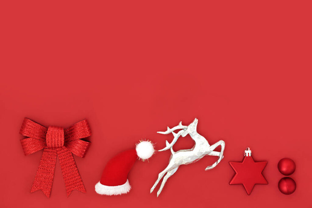 Kerstavond traditionele noordpool symbolen op rode achtergrond met kerstman hoed, rendieren, ster en bal bauble boom decoraties en boog. Leuke kerst spannende wens concept.   - Foto, afbeelding