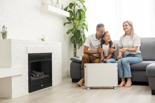 Electric heater at home. Young family warms near a heating radiator - Фото, зображення