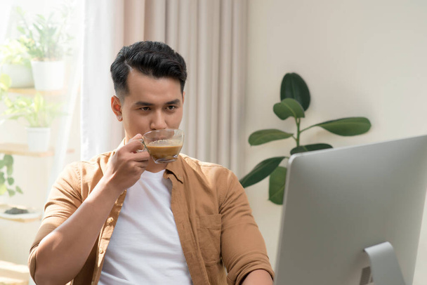 "Joven hombre de negocios que trabaja con PC, tomando café en el interior de la oficina blanca moderna. Hombre guapo, empleado exitoso en el trabajo con la computadora." - Foto, Imagen