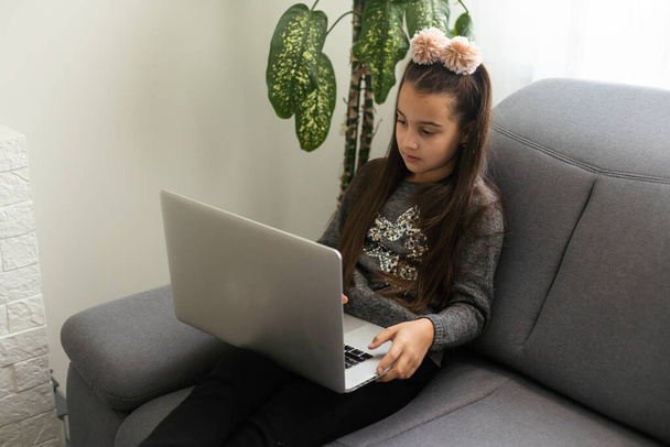 Caucasian Teenager girl, with a computer on a gray sofa in house - Photo, Image