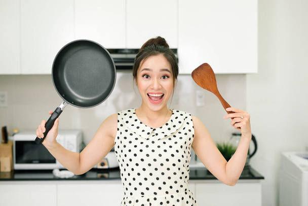 "Happy housewife hold up with pan wooden turner in kitchen" - Foto, Bild