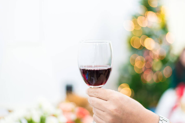Glass of red wine for toasting in party with Christmas tree background. Celebration and Anniversary concept. New year toast and Drinking concept - Fotó, kép
