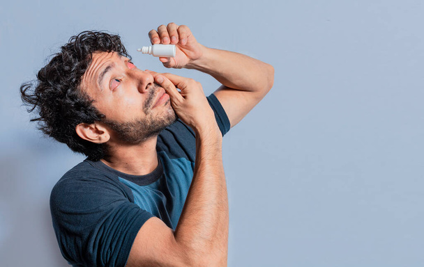 Person applying dropper to irritated eye. People applying refreshing drops to irritated eye. Man putting a dropper in his eye isolated. Man with irritated eye applying drops with a dropper - Photo, Image