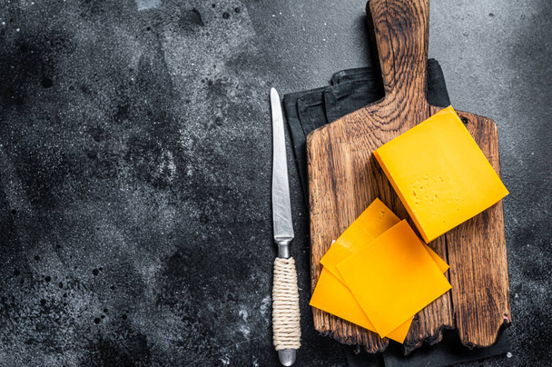 Slices Cheddar Cheese op een houten snijplank. zwarte achtergrond. Bovenaanzicht. Kopieerruimte - Foto, afbeelding