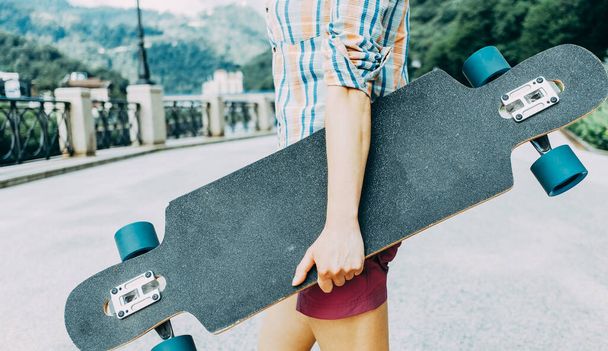 Onherkenbare tiener met longboard op straat - Foto, afbeelding