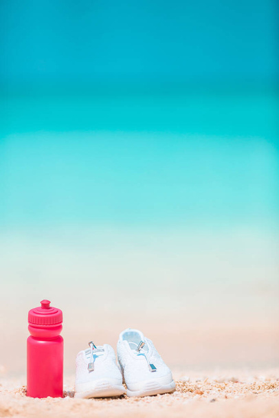 Спортивне взуття та пляшка на білому піщаному пляжі
 - Фото, зображення