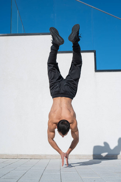 Man doing a handstand outdoors against a white wall - Fotó, kép