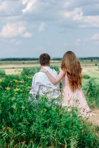"Rückansicht eines jungen Paares, das auf dem Hügel sitzt und ins Tal blickt" - Foto, Bild