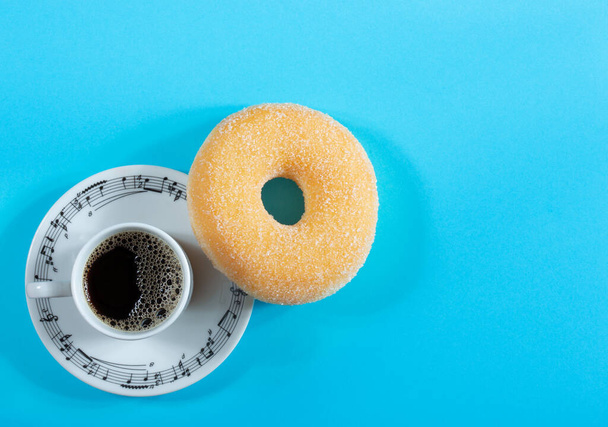 Coffee cup with musical sings and sugar donut on blue background - 写真・画像
