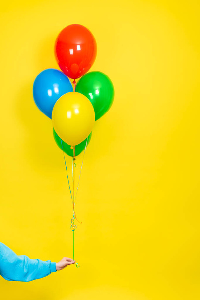 Kobieta trzyma w ręku kilka kolorowych balonów. Koncepcja imprezy lub prezentacji. Zielony, czerwony, żółty i niebieski Balony i ręcznie izolowane na żółtym tle - Zdjęcie, obraz