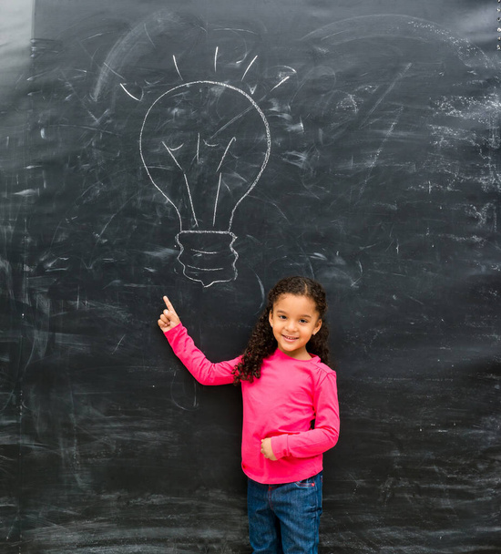 mosolygós kislány mutatva rajzolt a táblára lámpa - Fotó, kép