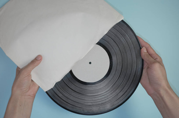 Hands hold an old vinyl record in an old paper case on a light blue background. - Foto, Imagen