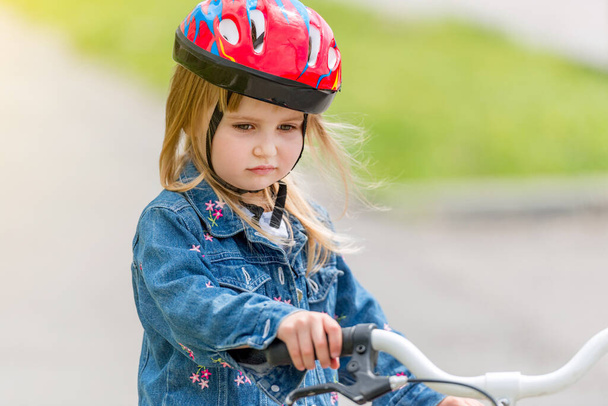 linda niña en casco y chaqueta de mezclilla en una bicicleta
 - Foto, Imagen
