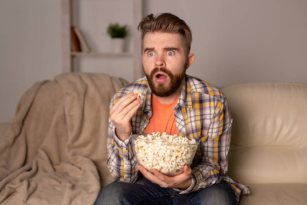 "Hombre barbudo viendo películas o juegos deportivos TV comiendo palomitas de maíz en casa por la noche. Cine, campeonato y concepto de ocio." - Foto, Imagen