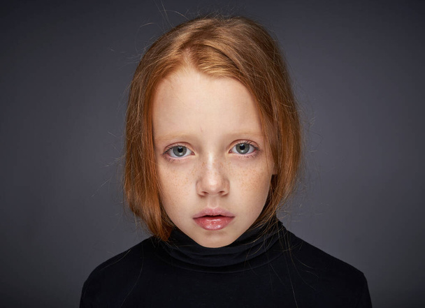 "red-haired girl with freckles on her face in a black sweater posing" - Foto, afbeelding