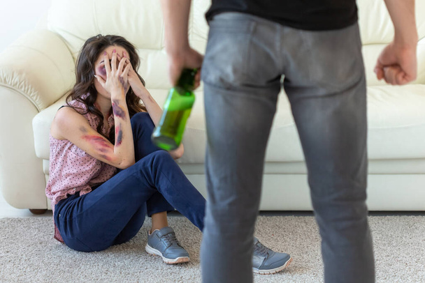 "家庭内暴力、アルコールと虐待の概念 - 床に座って彼の妻を虐待ボトルを持つ酔った男" - 写真・画像
