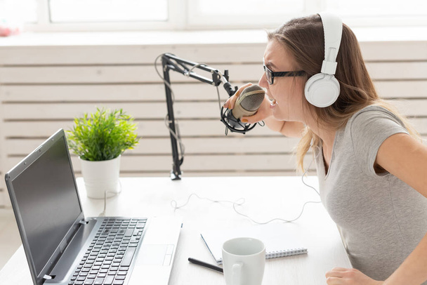 Koncepce rádiového hostitele-žena pracující jako rozhlasový hostitel, sedící před mikrofonem na bílém pozadí ve studiu - Fotografie, Obrázek