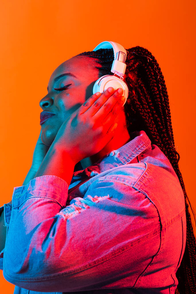 Neon-Porträt einer jungen schwarzen Frau hört Musik über Kopfhörer. - Foto, Bild