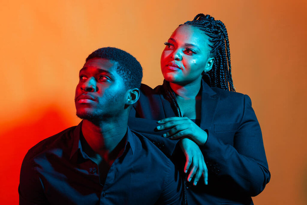 Portrait of young african american couple in love posing at studio dressed in classic clothes. Neon light. - Photo, Image
