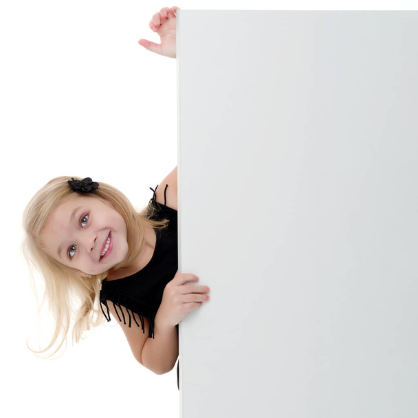 "Een klein meisje kijkt van achter een leeg spandoek." - Foto, afbeelding