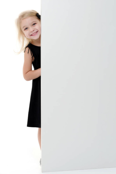 A little girl is looking from behind an empty banner. - Fotoğraf, Görsel