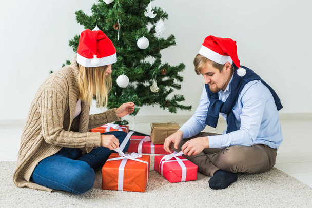 Holidays, relationship and festive concept - Couple opening present together by Christmas tree - Photo, Image