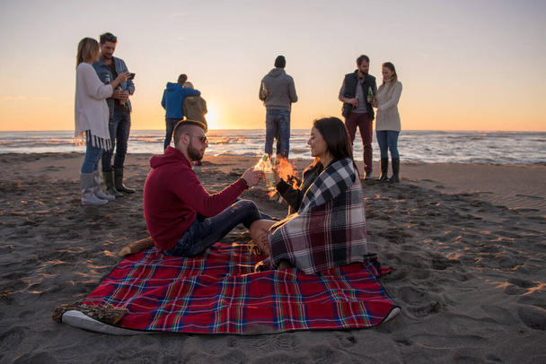 "Пара, наслаждающаяся закатом на пляже с друзьями" - Фото, изображение