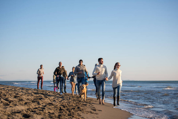 Ομάδα φίλων τρέχει στην παραλία κατά τη διάρκεια της ημέρας του φθινοπώρου - Φωτογραφία, εικόνα