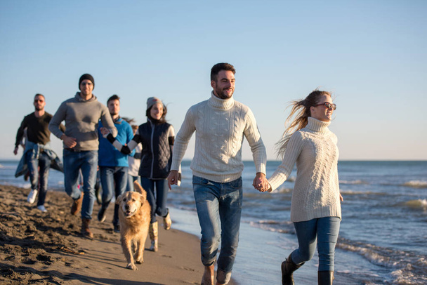 Group of friends running on beach during autumn day - Photo, Image