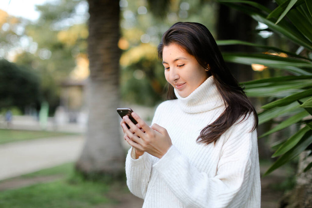 Корейская девушка с помощью смартфона и прогулки в тропическом парке. - Фото, изображение