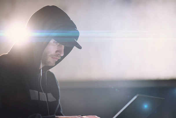 joven hacker talentoso utilizando el ordenador portátil mientras trabaja en la oficina oscura - Foto, Imagen