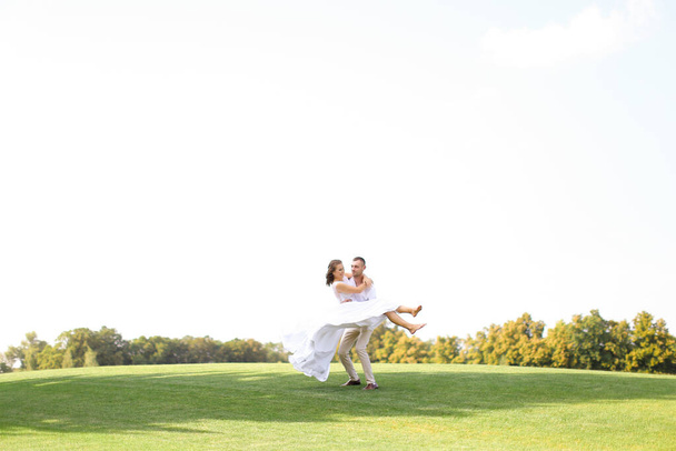 Groom holding bride on grass in white sky background. - Foto, afbeelding