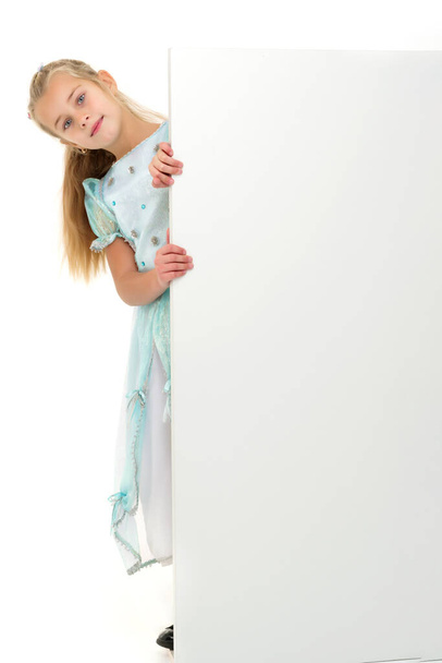 Een klein meisje kijkt van achter een leeg spandoek. - Foto, afbeelding