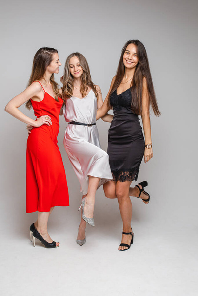 "Charming positive young girls friends wearing stylish feminine evening dresses posing on gray studio background" - Фото, изображение