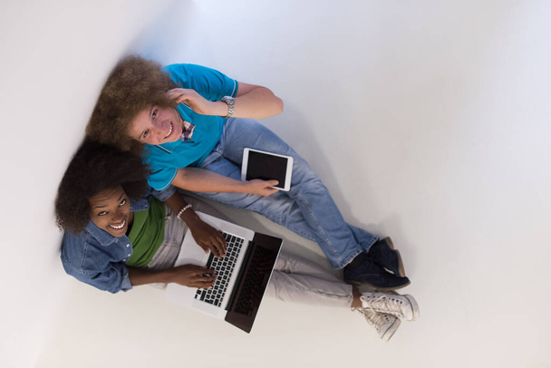 "wieloetniczna para siedząca na podłodze z widokiem na laptop i tablet" - Zdjęcie, obraz