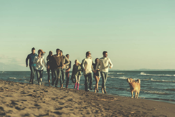 Grupo de amigos correndo na praia durante o dia de outono - Foto, Imagem