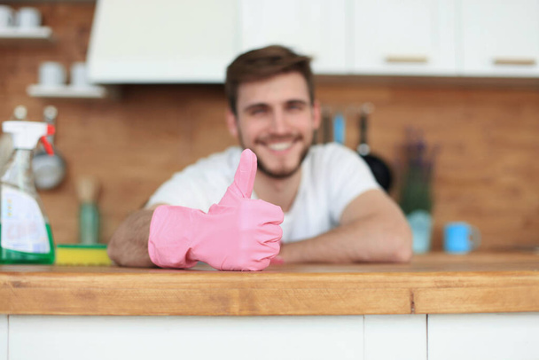 Νεαρός όμορφος χαμογελαστός άντρας καθαρίζει μοντέρνα κουζίνα. - Φωτογραφία, εικόνα