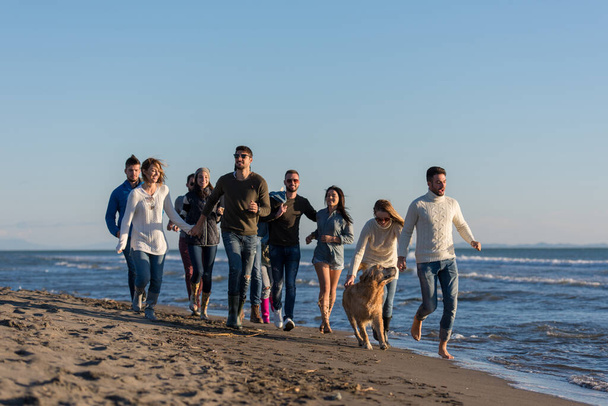 Grupo de amigos correndo na praia durante o dia de outono - Foto, Imagem