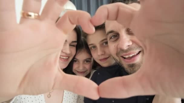 Egy nagy család a szív. Apa, anya és lánya egy szív alakú kézmozdulatot tesznek. A család a kamerába néz, nevet, bemutatja a családi szeretet fogalmát. Boldog család. - Felvétel, videó