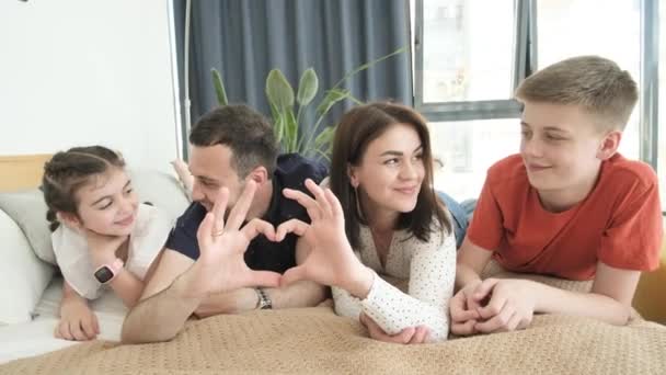 Egy nagy család a szív. Apa, anya és lánya egy szív alakú kézmozdulatot tesznek. A család a kamerába néz, nevet, bemutatja a családi szeretet fogalmát. Boldog család. - Felvétel, videó
