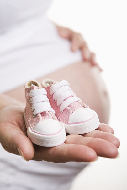 Pregnant woman holding baby shoes - Fotó, kép