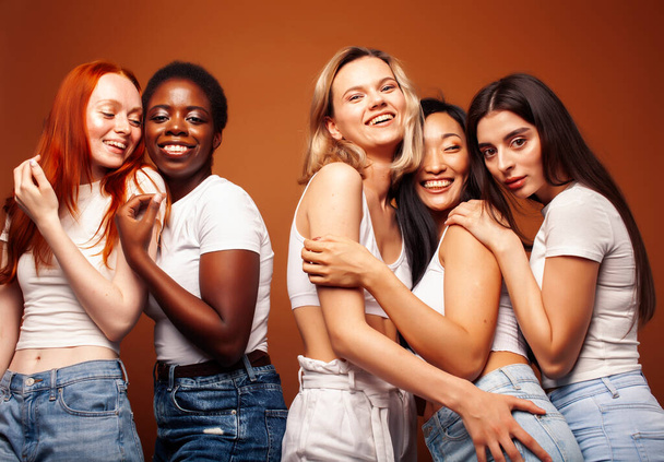 jonge mooie Afrikaanse en blanke vrouwen poseren vrolijk samen op bruine achtergrond, levensstijl diverse nationaliteit mensen concept - Foto, afbeelding